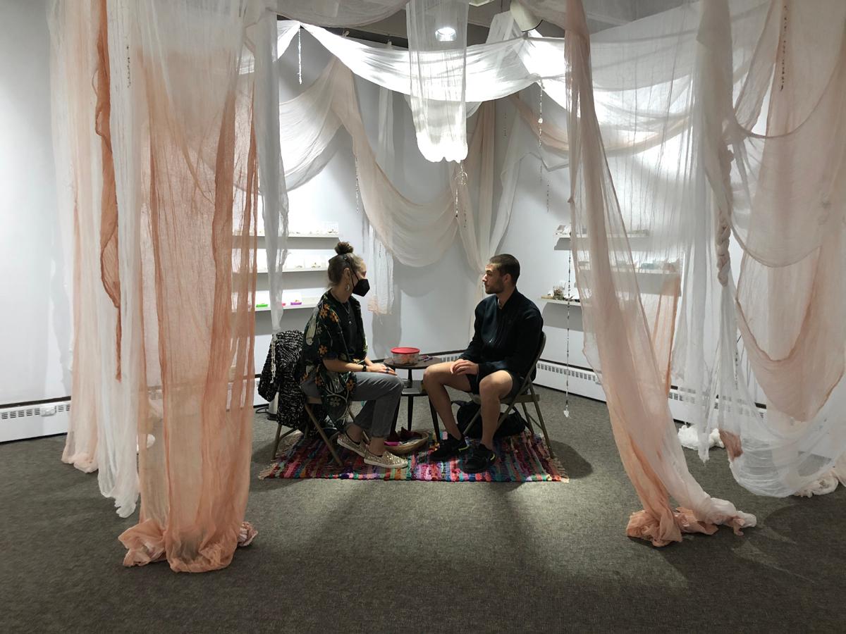 Two people sitting across from each other in chairs underneath sheer pale pink and white fabric.