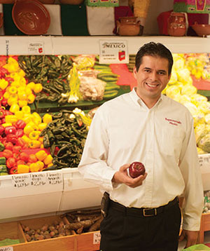 Javier Olvera posing in the produce department of his grocery store