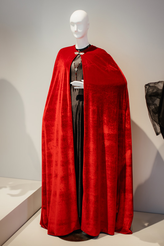 A photograph of a dress form draped with a rich red cape emboridered with starburst shapes