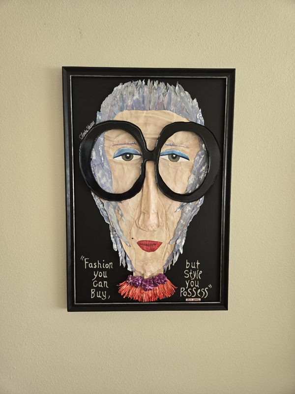 A paper mache cartoonish face of an older woman with bright red lipstick and blakc horn rimmed glasses