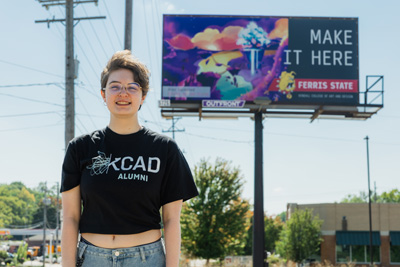 A young persion with short brown hair and a black t-shirt standing in front of a billboard