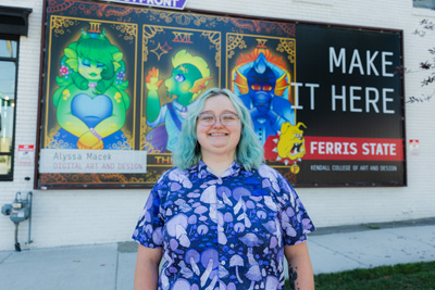 A young woman with dyed cyan hair and a flowered t-shirt standing in front of a billboard