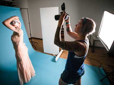 A woman holding a camera up to take a picture of a model in a flowing dress and sikver mask
