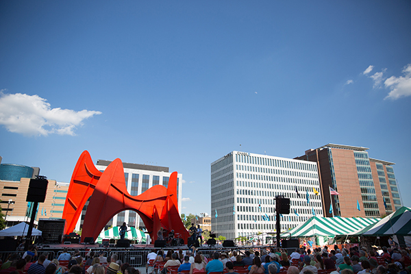 Large red sculpture with people dancing all around it