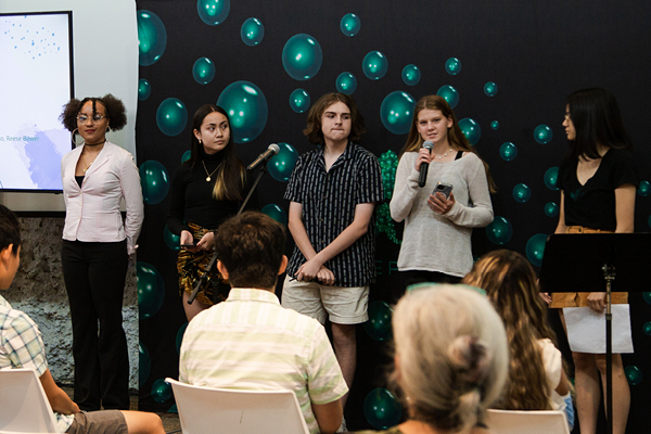 Three students standing in front of a black and green backdrop giving a presenation