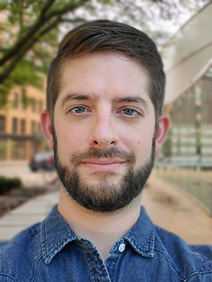 Portrait of a man with close-cropped brown hair, a brown beard, and a dark blue denim shirt