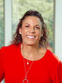 Photo portrait of a woman with curly brown hair wearing a bright red shirt and a golden necklace with a circular pendant