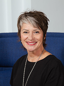Portrait of a woman with short-cropped black hair with streaks of white in it wearing a black shirt and a long chainnecklace