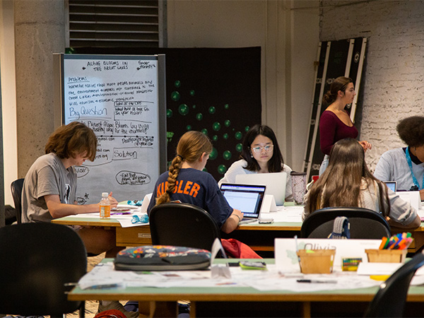 A group of high school students sitting around a table, working on laptops.