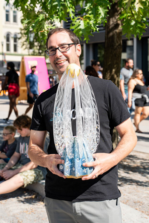 A person wearing a black t-shirt with KCAD logo holding a custom designed trophy.