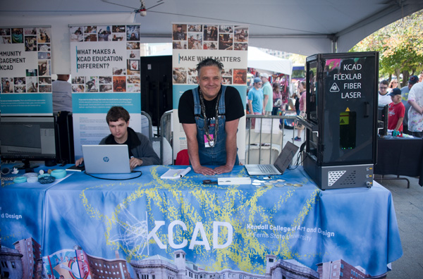 A person wearing overalls and smiling while hosting KCAD's Maker Expo Booth at Confluence Festival.