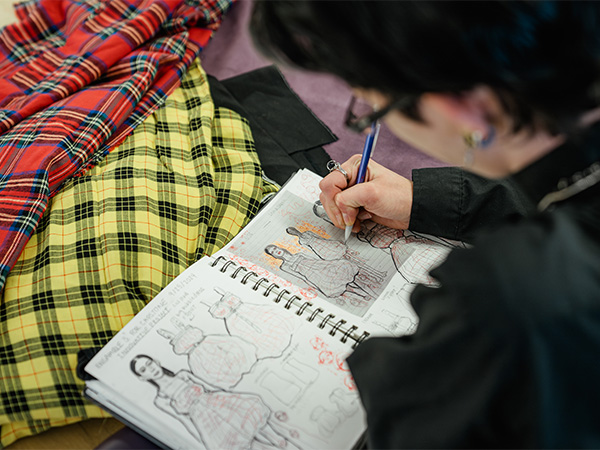 A student sketching fashion designs in a notebook.