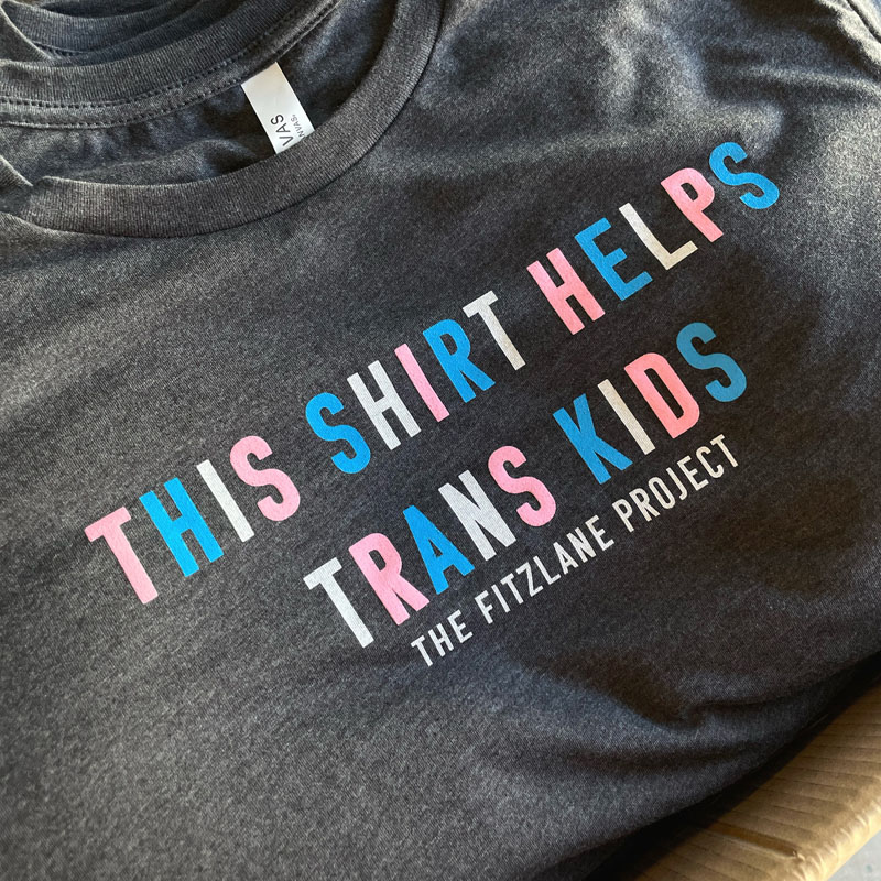 A screen-printed t-shirt reading this shirt helps trans kids