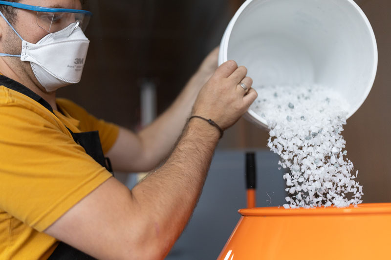 a man wearing an oragne shirt dumping shredded plastic waste into a bin