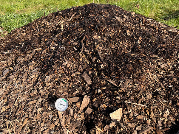 Pile of mulch on a green lawn with a meter inserted for material testing