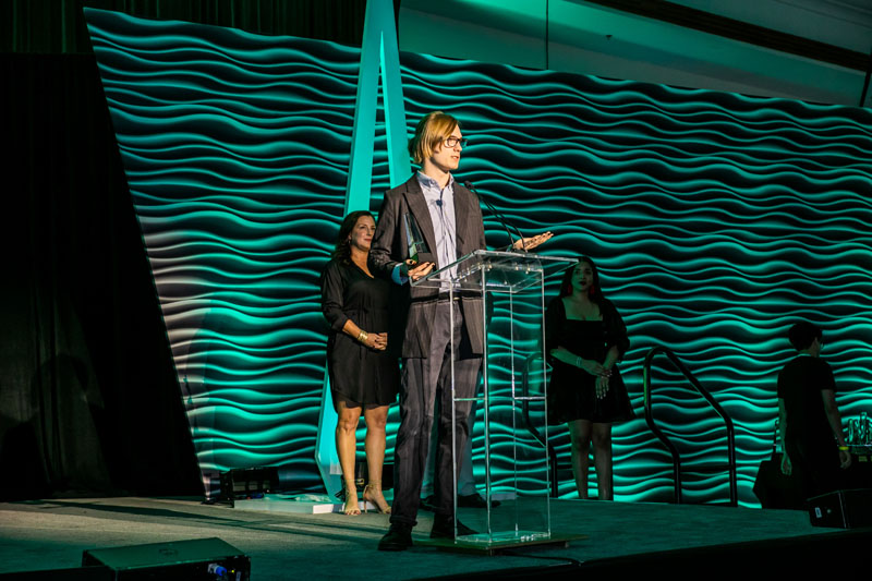 A young man in a suit standing at a podium holding a trophy