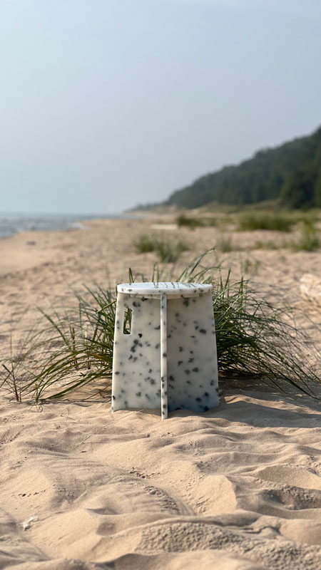 A white and black stool sitting on the beach next to the water