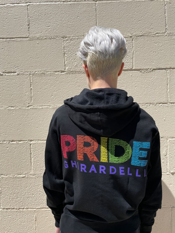 A shot of a person from the back wearing a black sweatshirt with the word pride in decorative rainbow colors. 