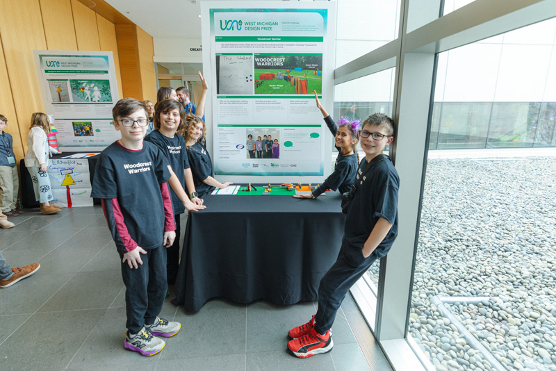 A group of young students posing next to an informational poster detailing their idea for a ninja warrior style obstacle course at their school