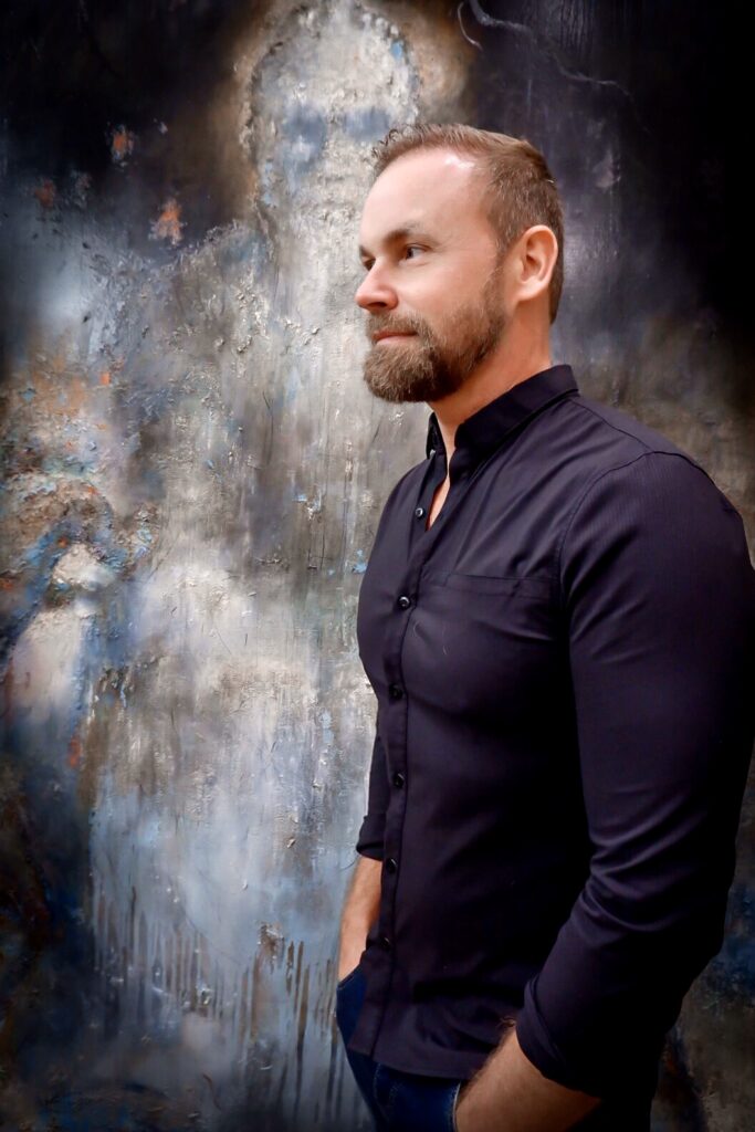 Photo of male artitst standing in front of large abstract painting