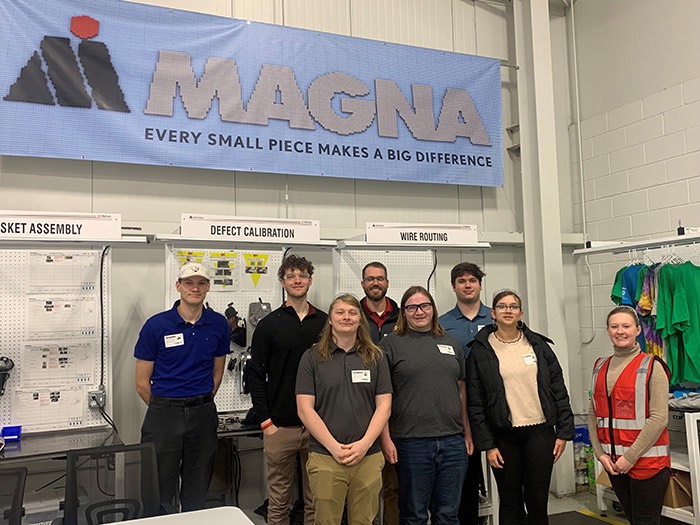 A group oif students standing in front of a Magna Mirrors banner