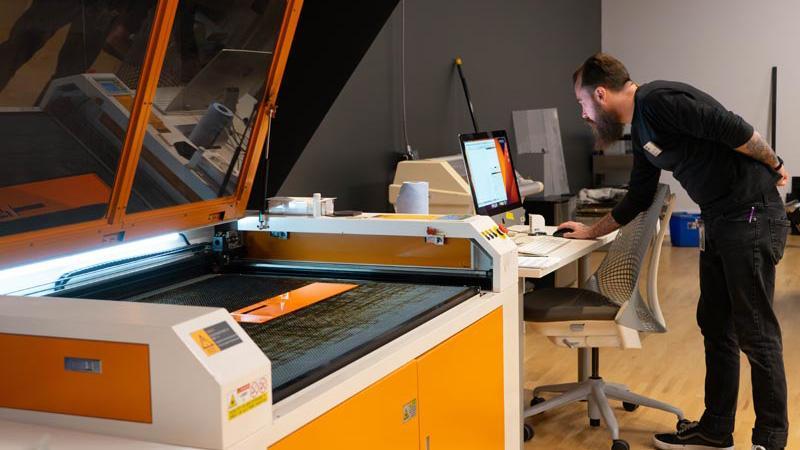 A man at a computer next to a large laser cutter