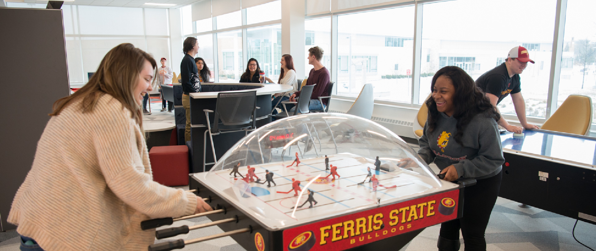 Students playing games, including bubble hockey, pool, and air hockey, in the lobby of North Hall, a residence hall on the campus of Ferris State University in Big Rapids, MI
