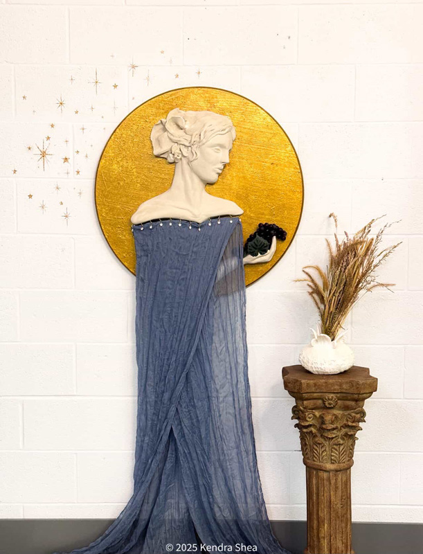 A photograph of a cermic bust affixed to a wall with a light purple gown flowing from its bottom edge
