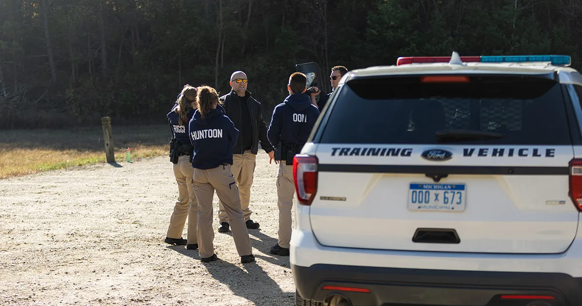 Students listening to professor outside near cop car