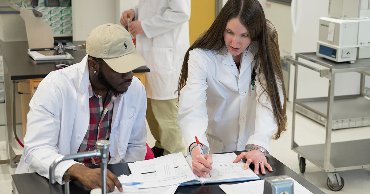 A Ferris State University Forensic Biology student sitting in an indoor lab reviewing lab materials with a Forensic Biology faculty member.