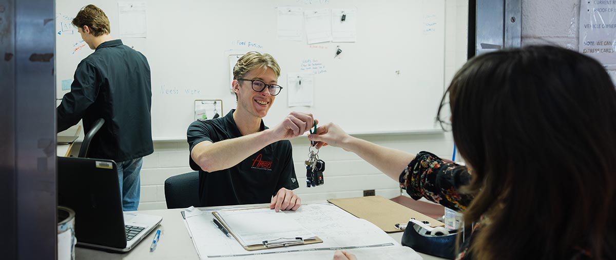 automotive management student handing keys to another student