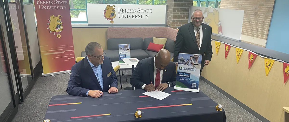 men sitting at a table signing an agreement with ferris state bulldog signage around them