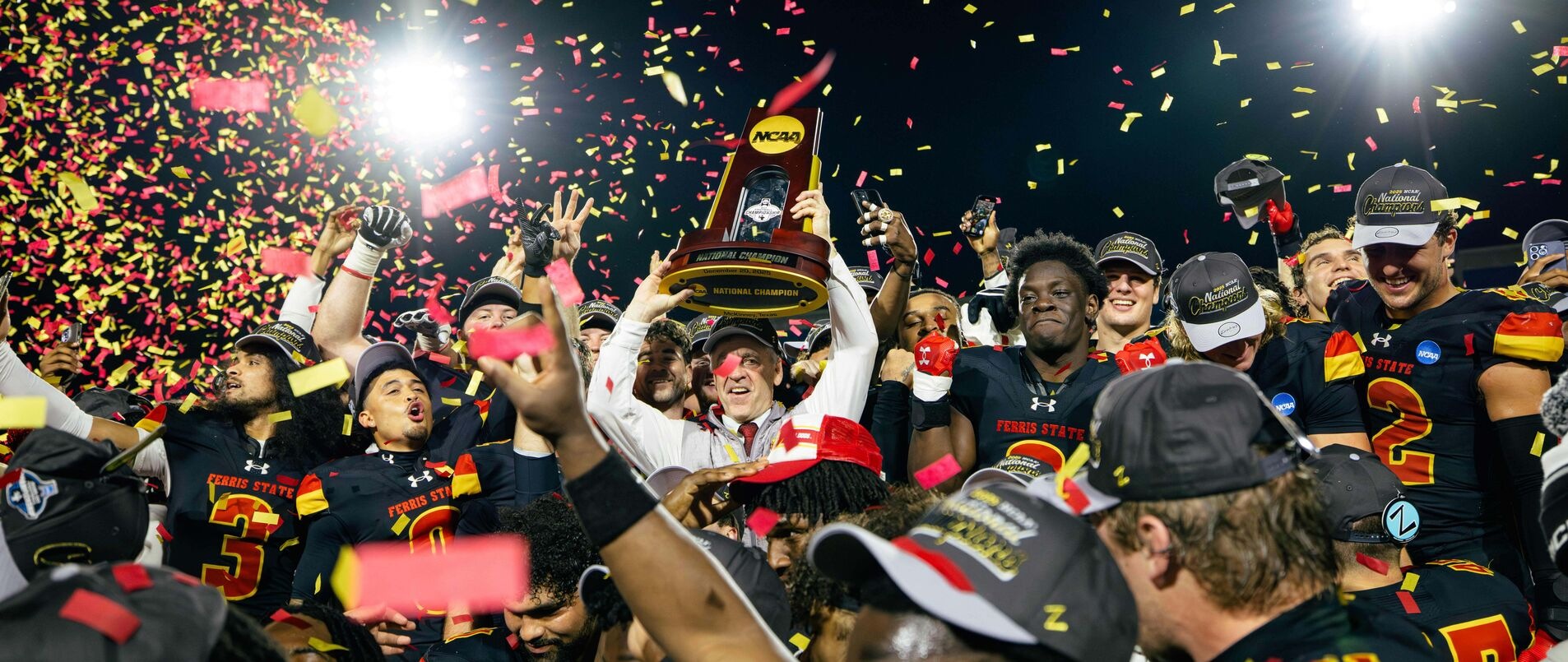 Football team holding NCAA Championship trophy among confetti