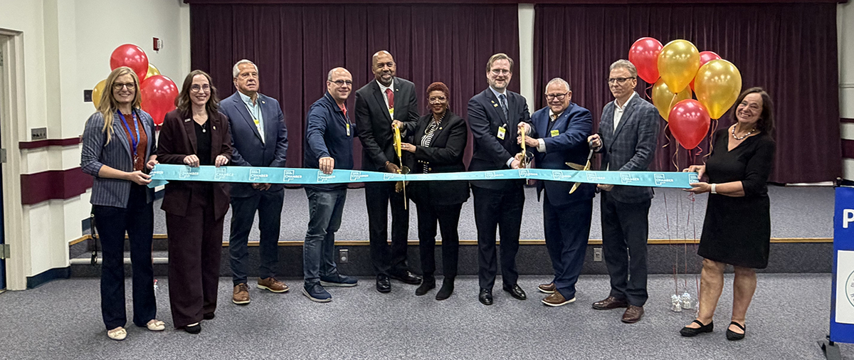 a group of people holding a large ribbon with two people in the middle holding large scissors