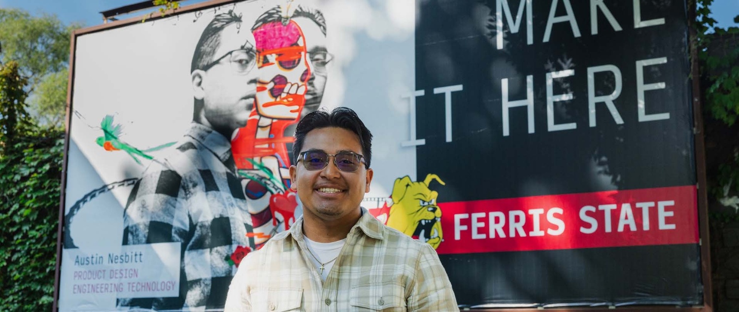 KCAD student Austin Nesbitt standing in front of a billboard inspired by his design