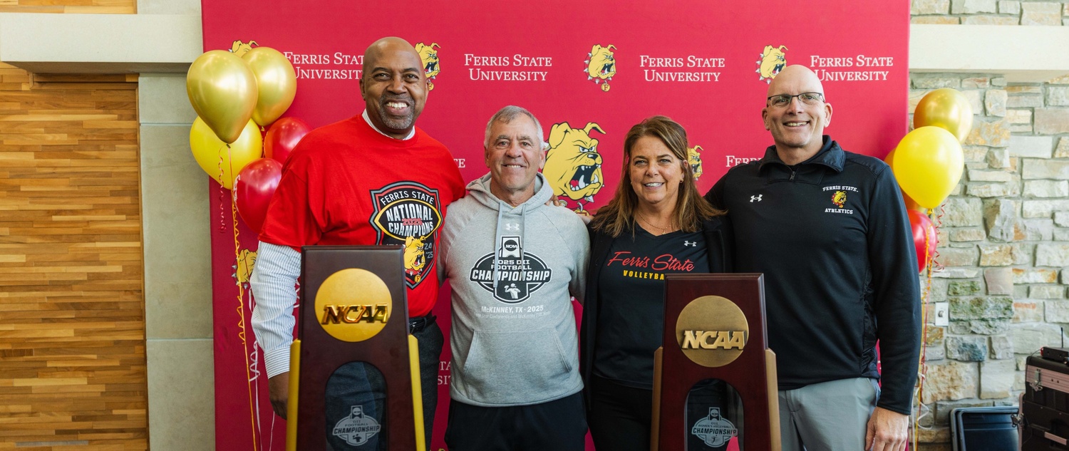 Ferris State President Bill Pink, football head coach Tony Annese, volleyball head coach Tia Brandel-Wilhelm, and Athletics Director Steve Brockelbank posing in front of the recent NCAA trophies