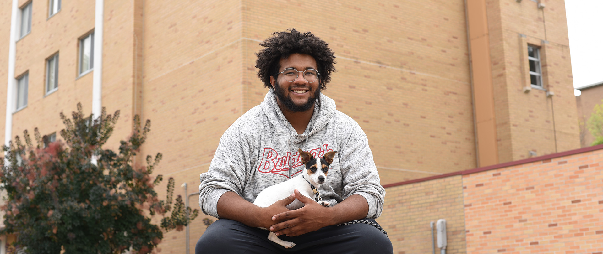 Student with their pet dog in front of a student residence hall at Ferris State University, the site of a pet-friendly floor in a student residence hall