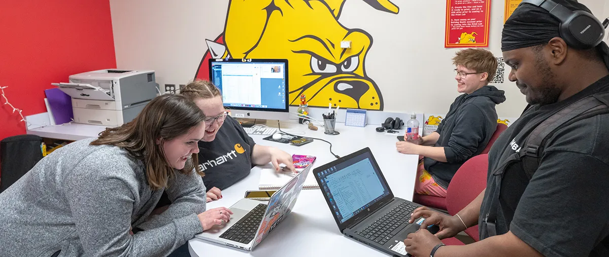 four students working on computers in an office