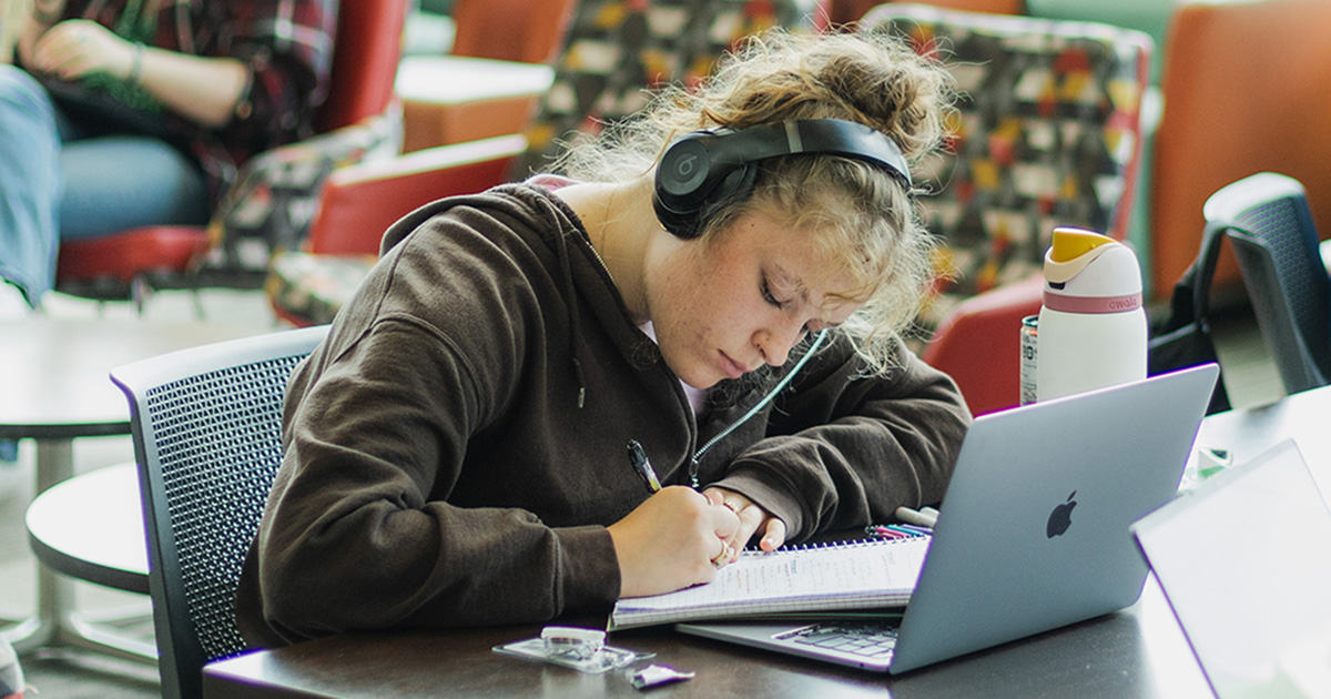 Student studying writing on a note pad and wearing headphones