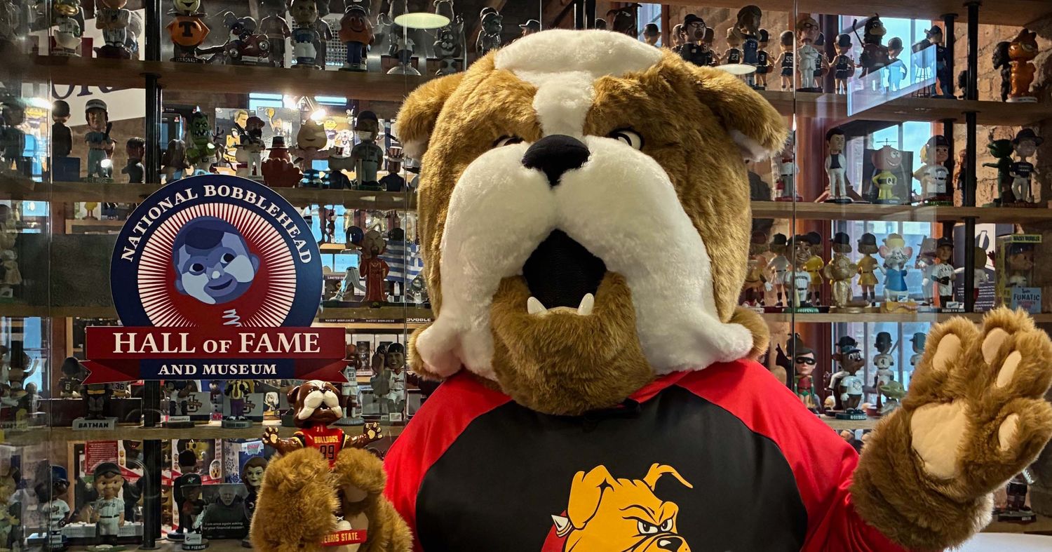 Brutus holding his bobblehead next to the National Bobblehead Hall of Fame and Museum logo