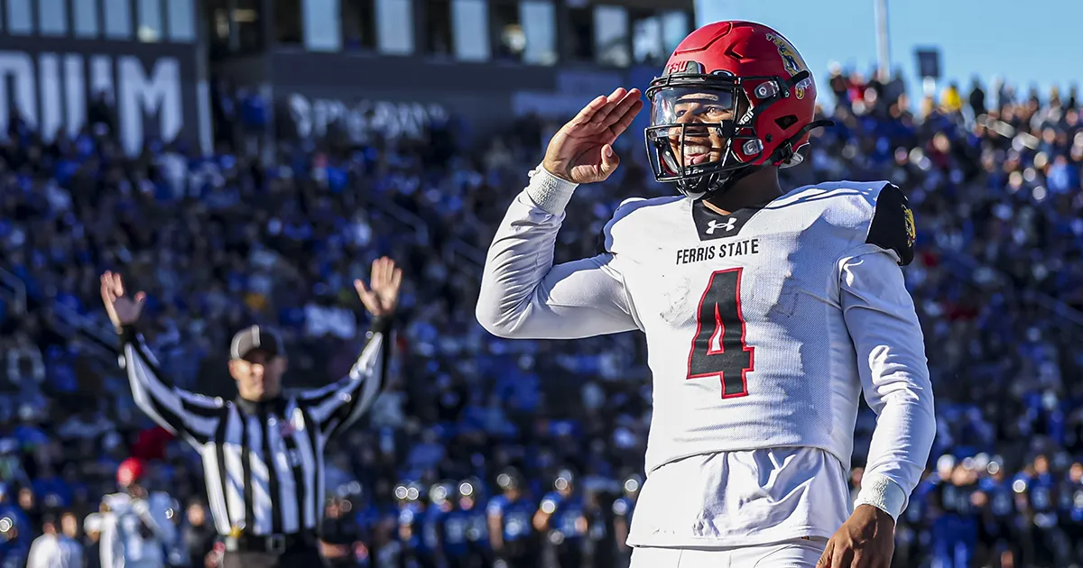 football player salutes with a referee in holding up touchdown arms in the background