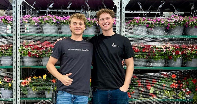Henry Mast posing with a colleague in front of a display of flowers.