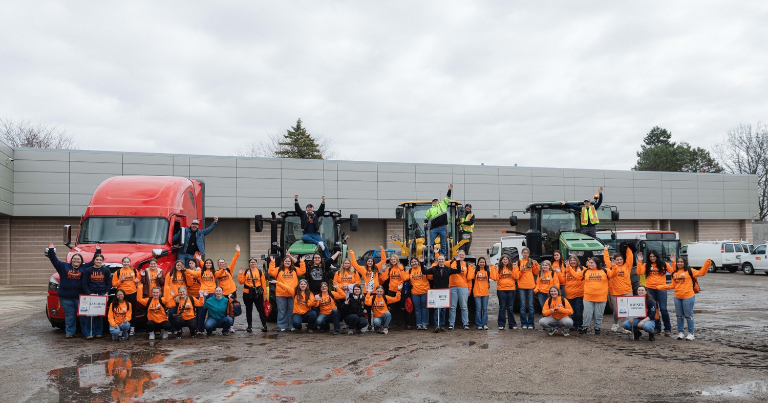 A large group of the high school students posing in front of large vehicles outside of Ferris State's Heavy Equipment hall