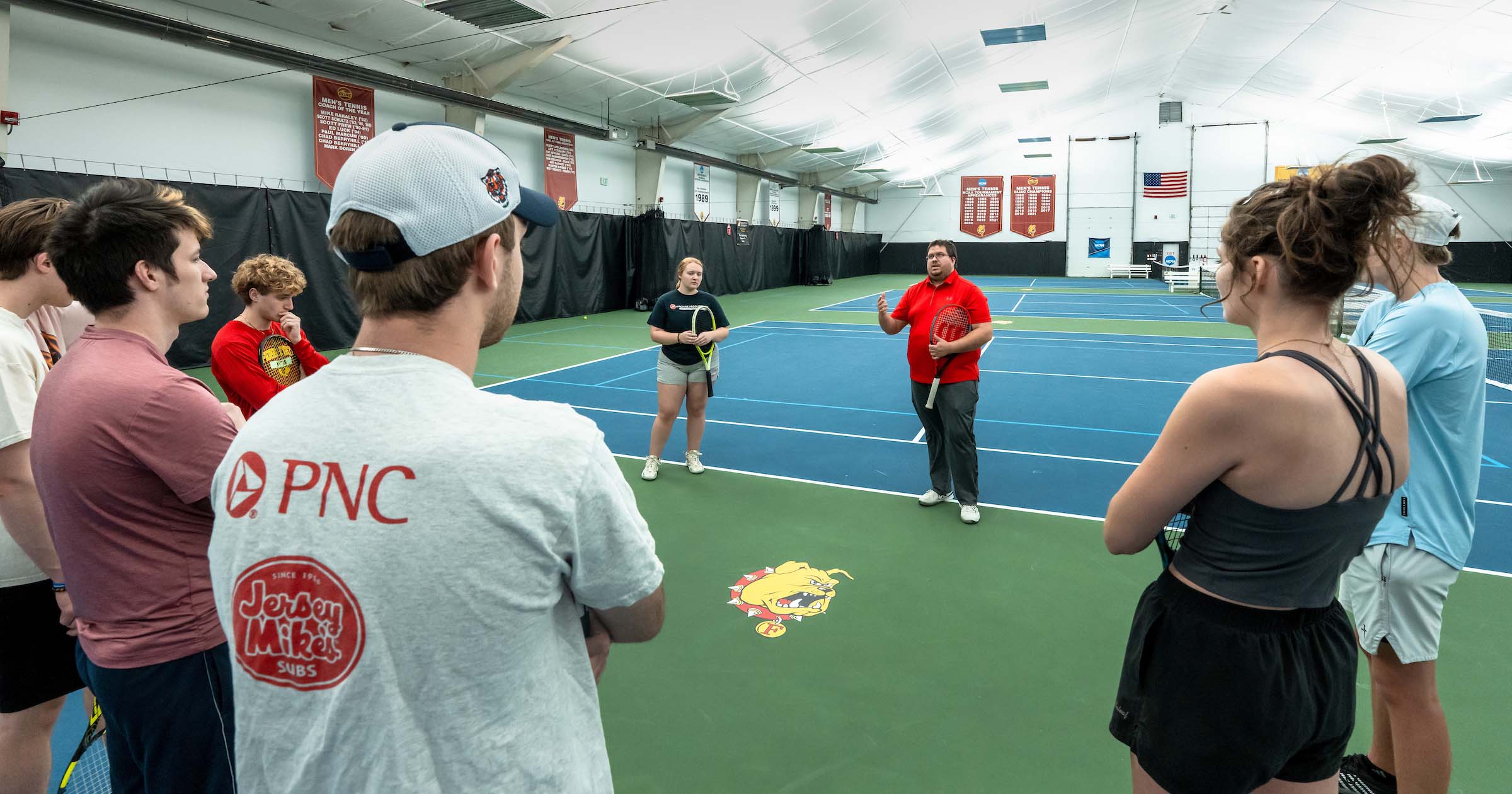 Michael Janz, Assistant Director of Ferris State University’s Professional Tennis Management, and students during instruction on the court.