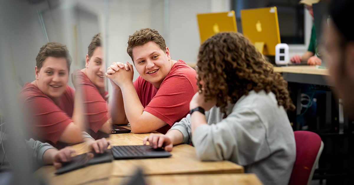 two students talking in a classroom in front of computers