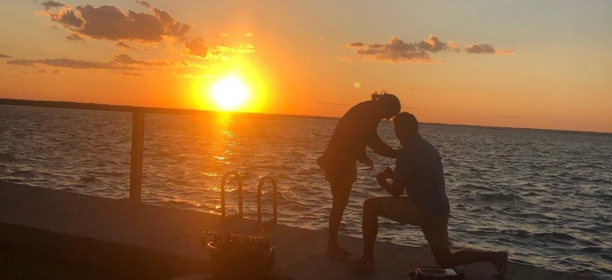 Cole proposing to Olivia at the waterfront with the sun setting behind them