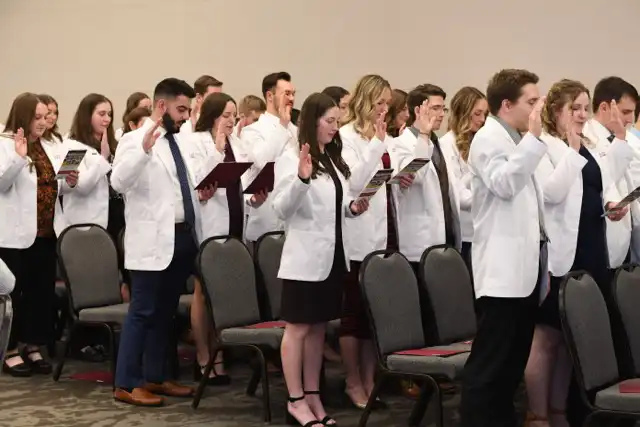 Students in white coats holding up their right hands