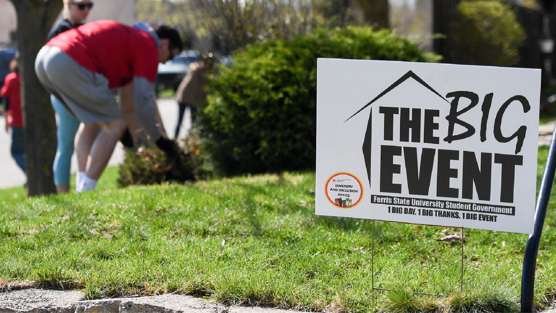 Student raking with BIG event poster in front yard