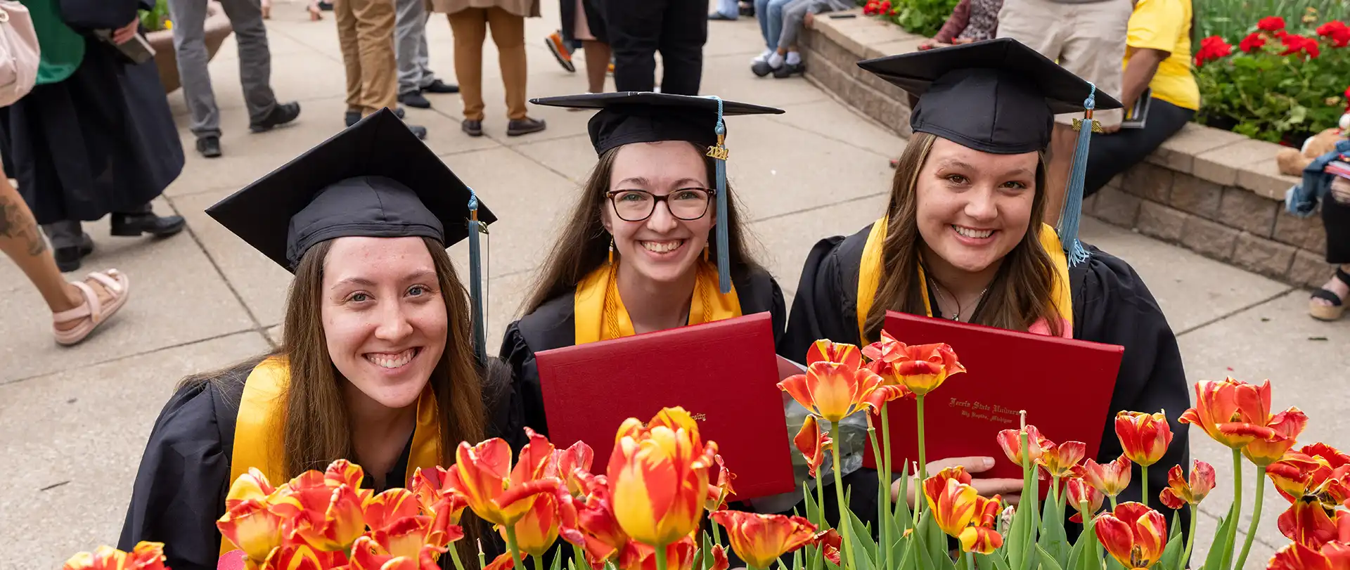 Graduating students holding diplomas amid flowers